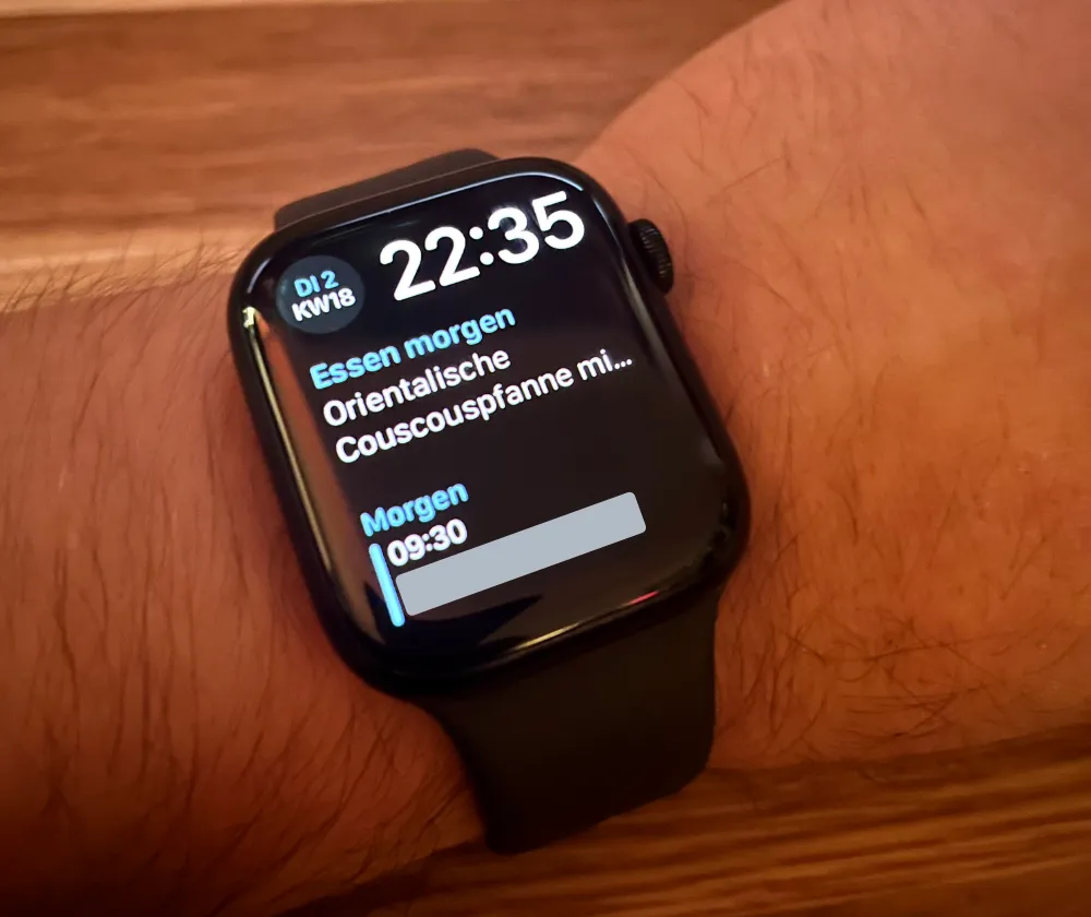 Apple Watch on a wrist showing the time 22. Below the time, a complication reads "Essen morgen" (meal for tomorrow) with the text "Orientalische Couscouspfanne mi..." and a calendar entry showing "Morgen 09"